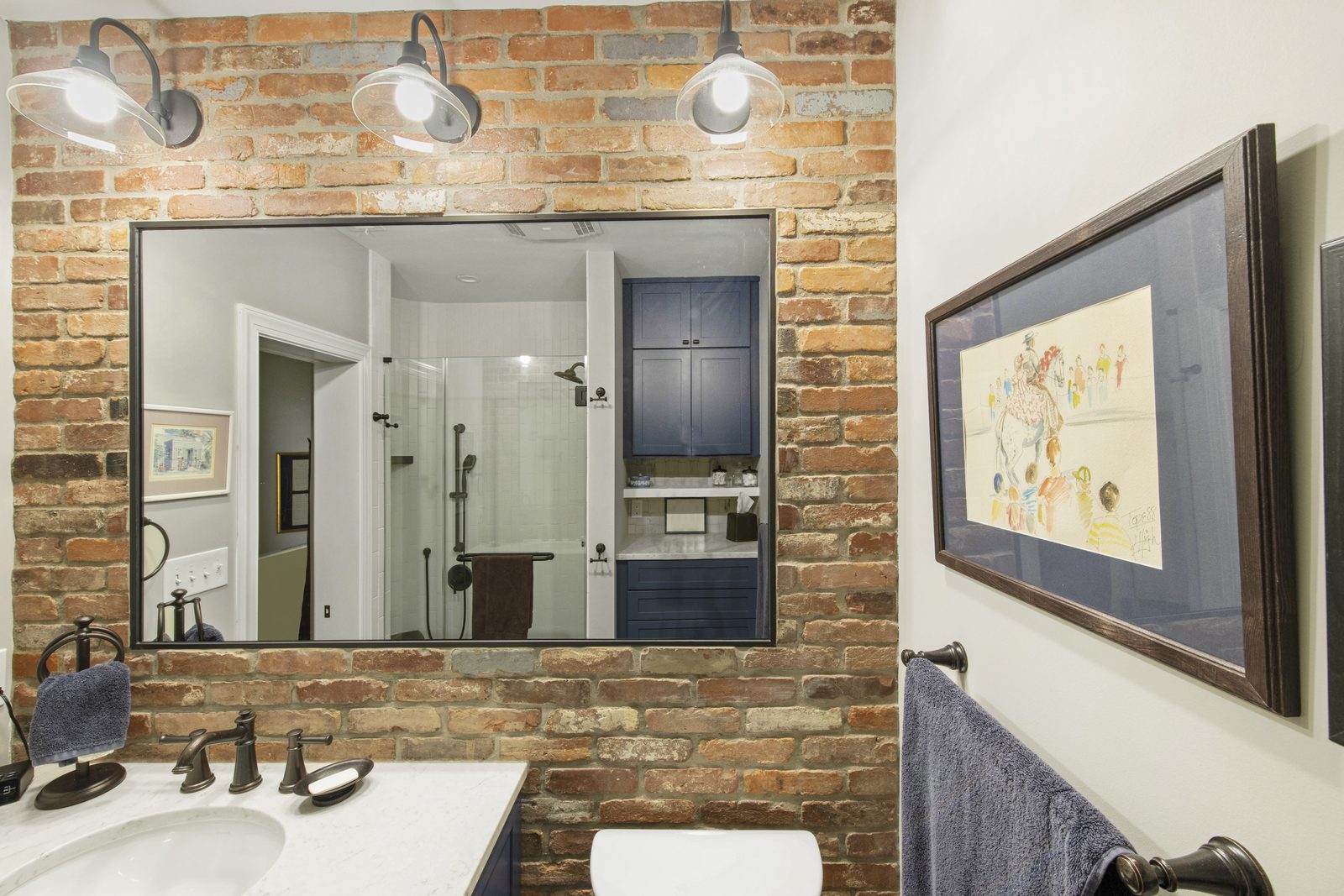 Bath with brick accent wall, vintage mirror with industrial wall sconces, marble vanity