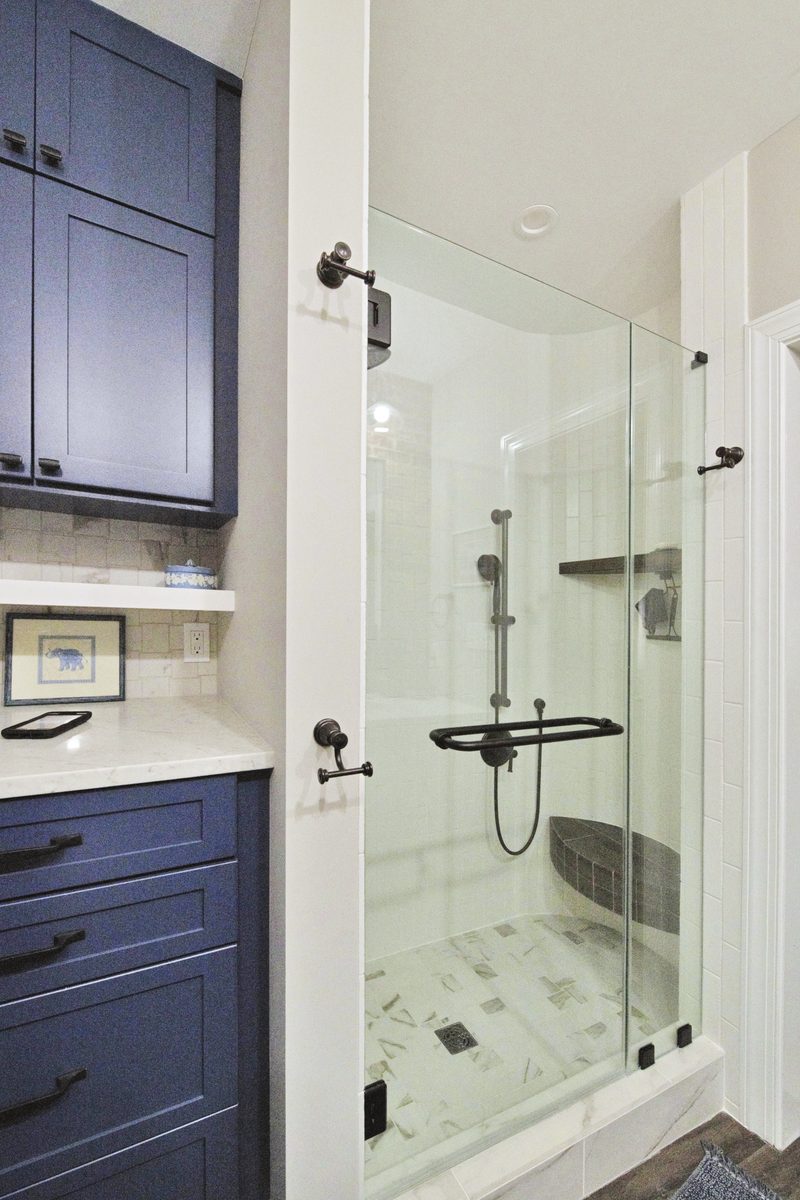Walk-in shower — frameless glass enclosure, marble pattern floor, navy shaker cabinetry