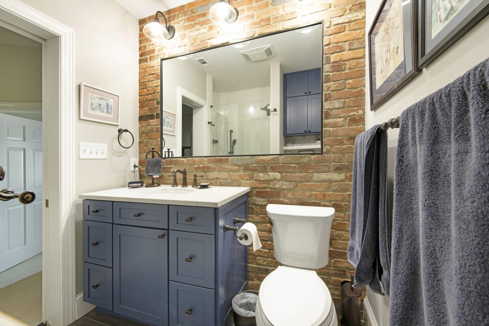 Bath — exposed brick wall, navy vanity with brass fixtures, framed artwork, plush towels