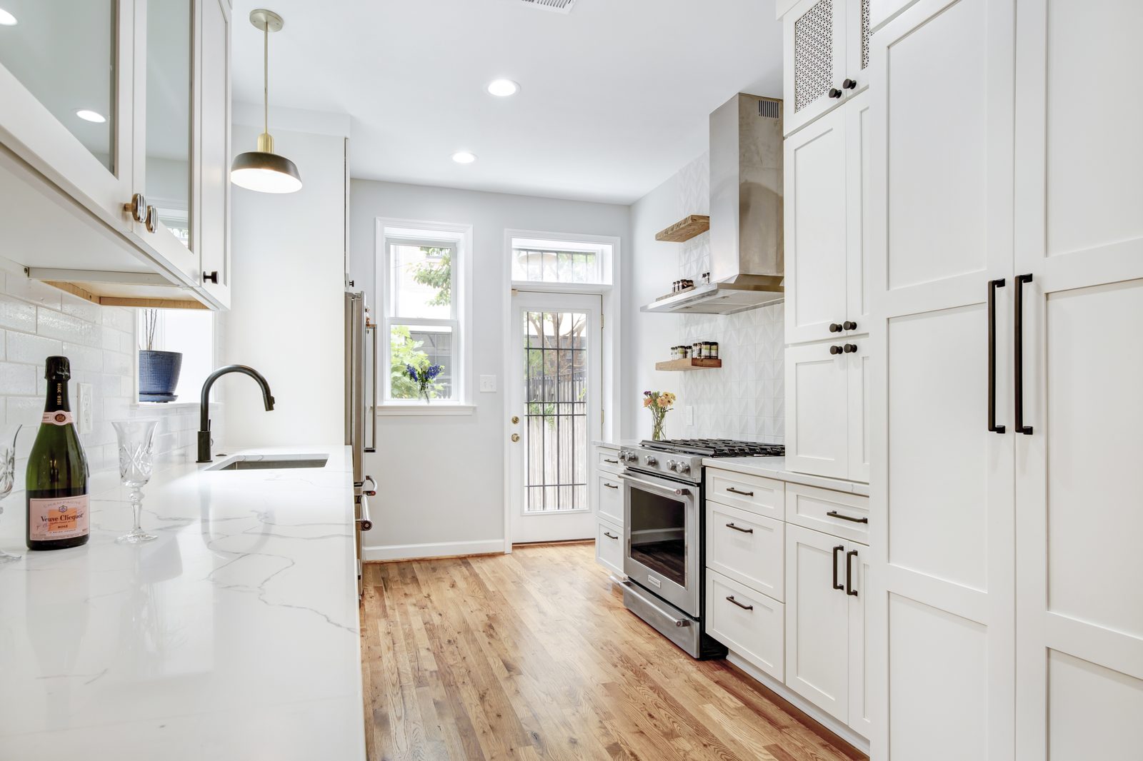 Chef's kitchen — white shaker cabinets, marble countertops, gas range with hood, hardwood floors, door to back garden