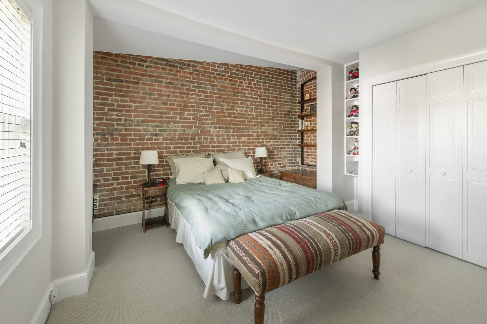 Bedroom — exposed brick accent wall, queen bed with mint linens, striped upholstered bench