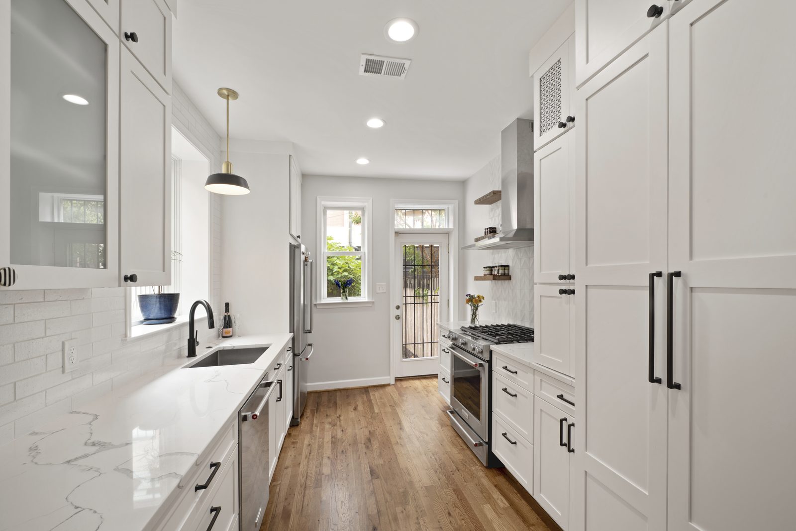 Galley kitchen leading to back door — white cabinetry, pendant lighting, stainless appliances, French door to garden