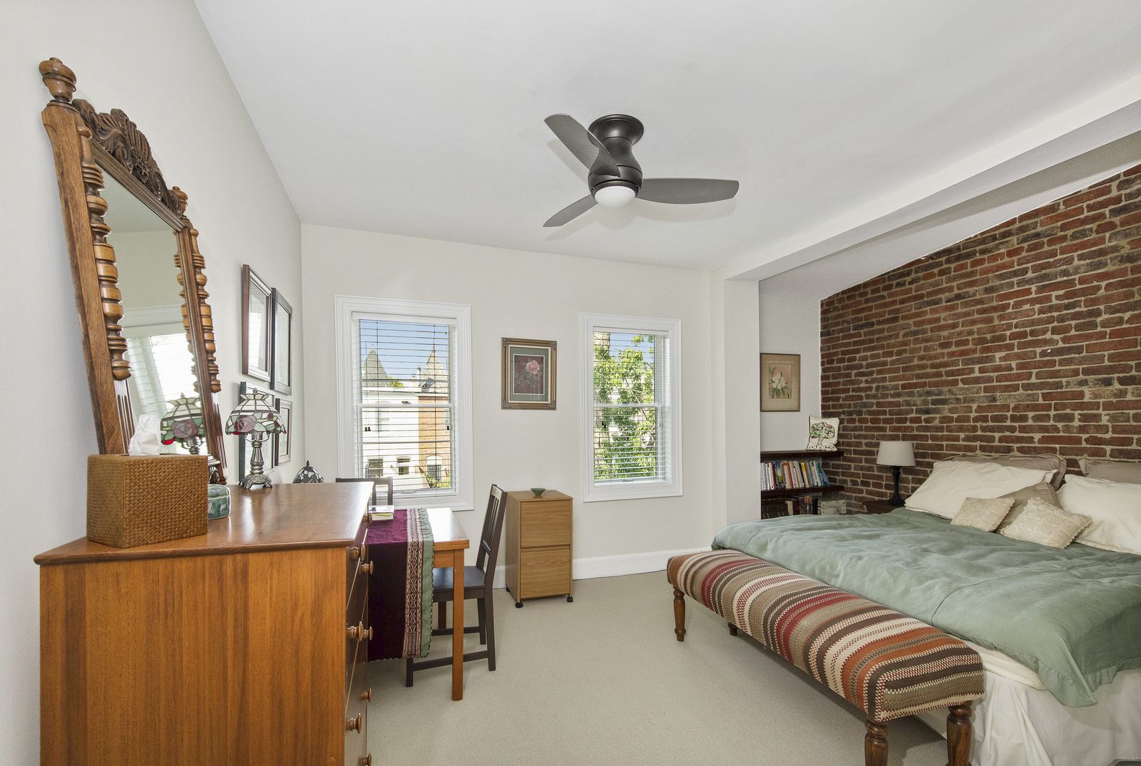 Bedroom with vintage carved mirror, wood desk, brick accent wall, twin windows